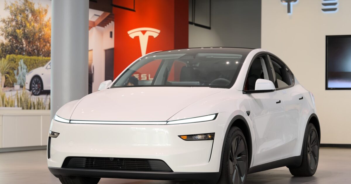 White Tesla Model Y Juniper on display at a Tesla showroom with Tesla logo in background