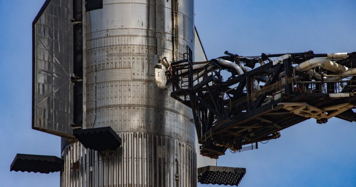 A SpaceX Super Heavy booster beside the launch tower quick-disconnect arm at Starbase