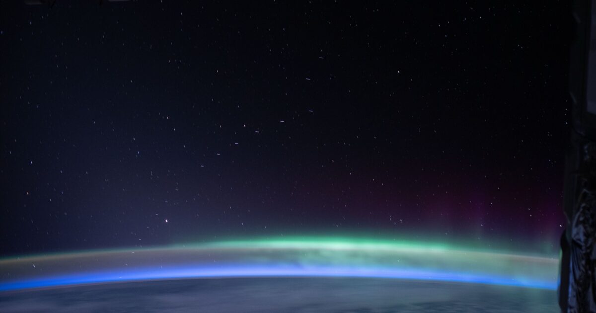 Starlink satellite train above Earth's glow and aurora as seen from the International Space Station