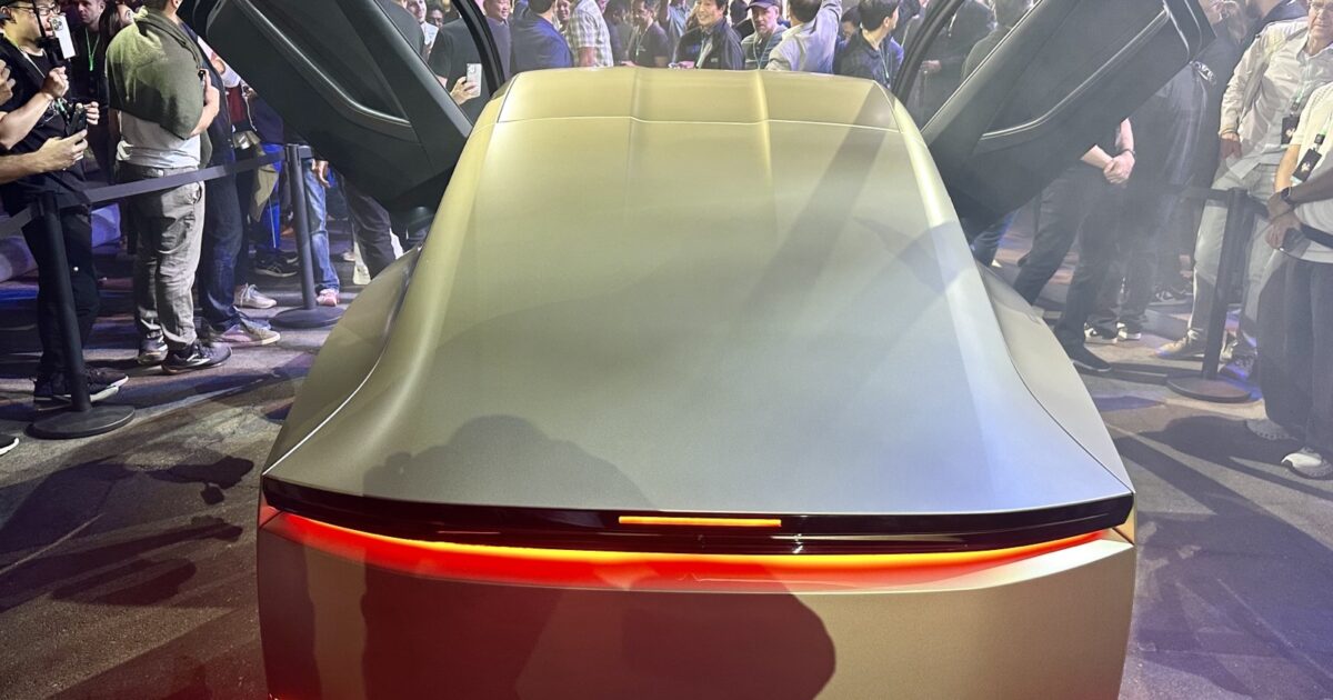 Rear three-quarter view of a gold Tesla Cybercab with both butterfly doors open