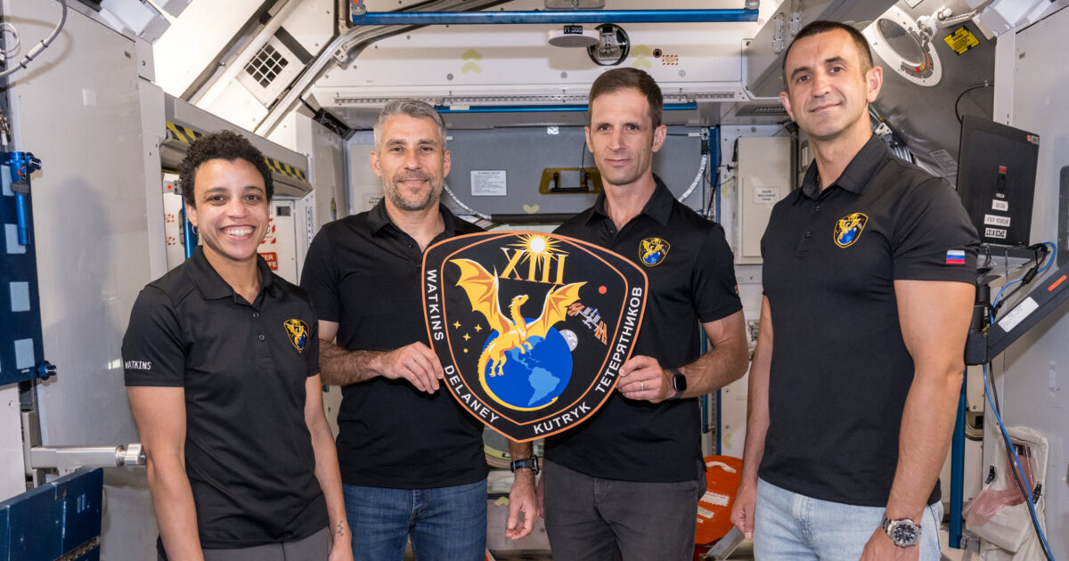 The four SpaceX Crew-13 astronauts holding their mission patch inside a training module