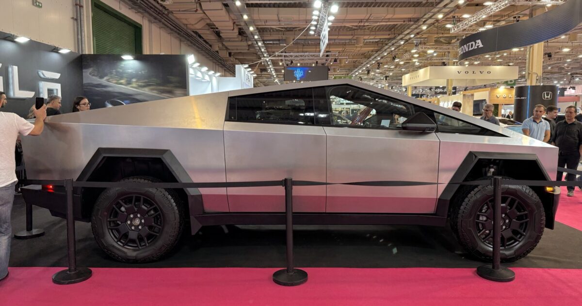 Side view of a stainless-steel Tesla Cybertruck at an auto show