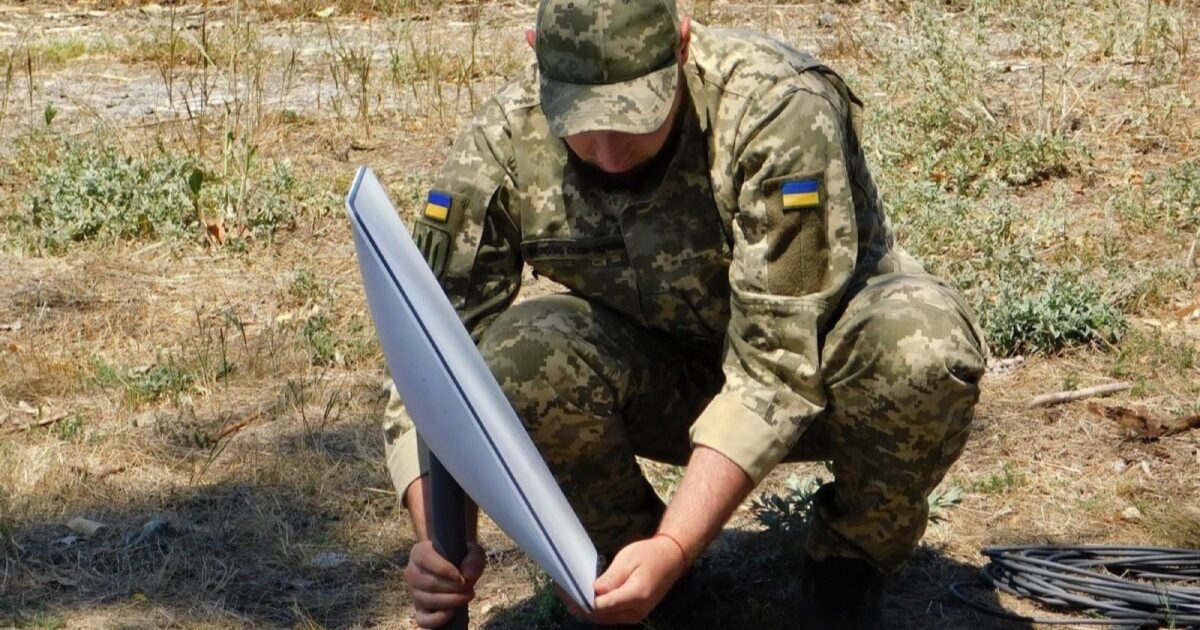 Ukrainian soldier installing a Starlink satellite terminal in a field